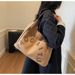 Close-up of khaki canvas tote bag with brown leather letters carried by a model