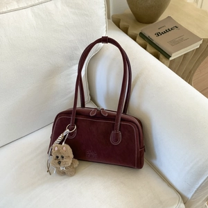 Detail of burgundy leather shoulder bag with white stitching and plush dog charm