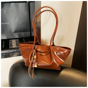 Detail of a brown leather tote bag with woven fringe tassel and a metal lock buckle