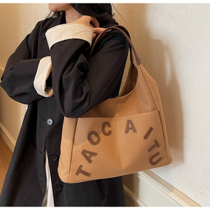 Detailed view of brown canvas tote bag with leather straps and logo patch on model