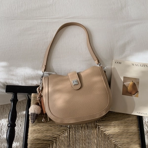 Close-up of beige saddle bag with lychee texture and silver buckle on a chair