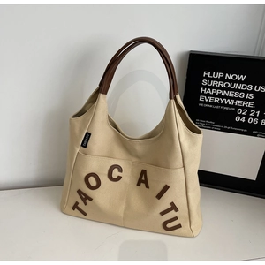 Detail of beige canvas tote with brown leather handles and TAOCAITU lettering