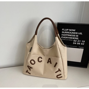Close-up of beige canvas tote with brown leather letter patches and reinforced handles