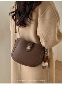 Detail of a brown lychee leather saddle bag with silver buckle and acorn charm decoration
