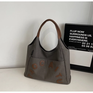 Close-up of dark grey canvas tote bag with brown leather straps and letter patch detail