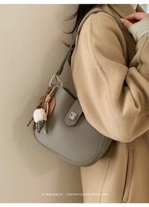 Detail of grey pebble leather saddle bag with silver twist lock and fashion charm on coat