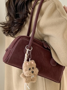 Chic burgundy bowling bag with white stitching and plush dog charm on shoulder