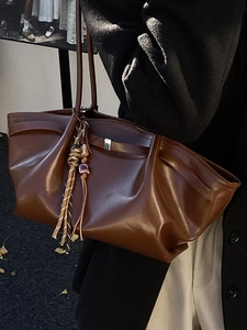 Large dark brown tote bag with pleated design and decorative woven charm on shoulder strap