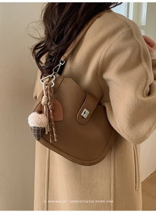 Detail of a brown leather bucket bag with silver metal buckle and cute plush charm pendant
