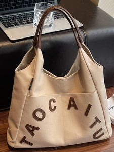 Minimalist canvas tote bag with brown leather handles and large letter collage design