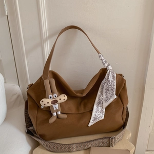 Detail of a brown suede tote bag with a patterned strap and decorative scarf