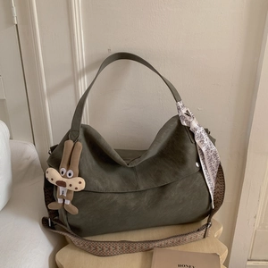 Detail of olive green tote bag with woven shoulder strap, scarf, and rabbit charm