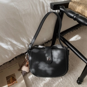 Detail of black lychee grain leather bucket bag with silver buckle and plush ice cream charm