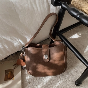 Close-up of brown textured leather bucket bag with metal buckle and heart charm detail