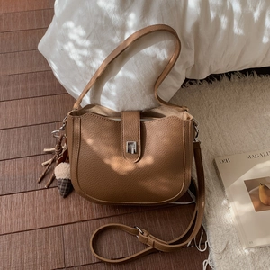 Close-up of a brown saddle bag featuring a T-shaped metal buckle and tassel on white rug