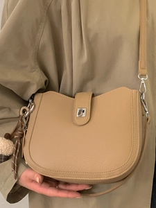 Minimalist beige pebble leather bucket bag with silver twist lock and plush charm accessory