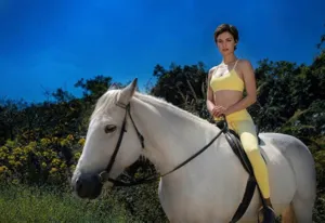 Outdoor shot of a lemon yellow sports bra and leggings set worn by a rider on a white horse