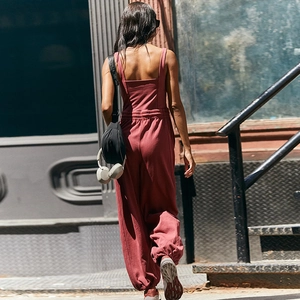Back view of a burgundy sports jumpsuit with elastic waist and jogger cuffs in street setting