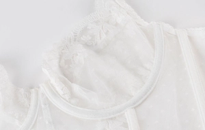 Détail de la dentelle florale brodée et du tulle à pois sur un bustier blanc