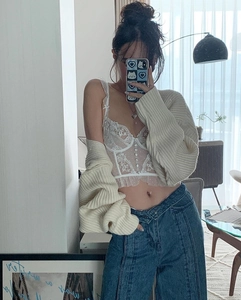Détail d'un bustier en dentelle blanche porté avec un gilet en maille et un jean bleu