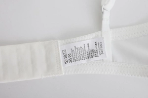Detail view of garment care label on white breathable mesh bra showing material composition