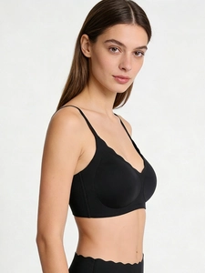 Detail of seamless black V-neck bra with wavy laser-cut edges and adjustable straps