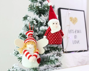 Close-up of plush Santa Claus and winged angel ornaments hanging on a snowy Christmas tree
