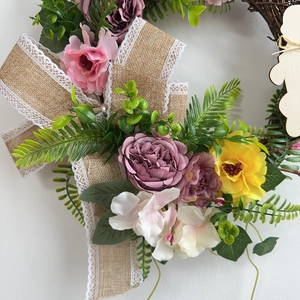 Easter rabbit wreath with colorful silk flowers and lace burlap bow on white wall