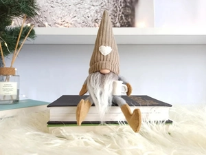 Detail eines gestrickten Weihnachtswichtels mit Kaffeetasse, der auf Büchern sitzt