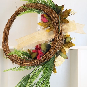 Handgefertigter Flechtkranz mit roten Kunstblumen und Herbstlaub auf weißem Holzhintergrund