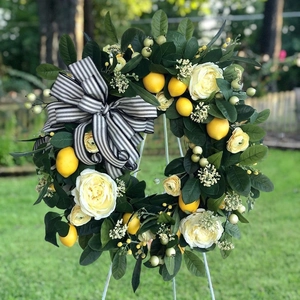 Close-up of yellow lemons and white roses on a green summer wreath with a striped bow