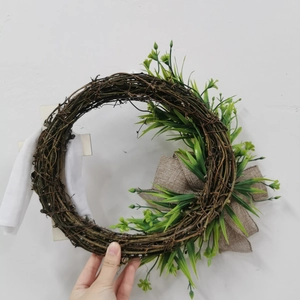 Detail of a rustic Easter vine wreath with green leaves, burlap bow, and white cross