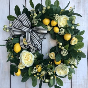 Detail of faux lemon and rose wreath featuring greenery and striped ribbon on wood