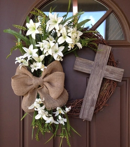 Easter cross wreath with white lilies, burlap bow, and greenery on dark wood door