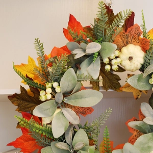 Close-up of autumn wreath detail with cream pumpkins, orange maple leaves, and white berries
