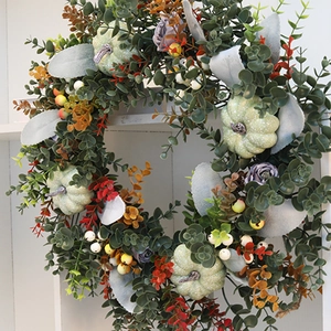 Detailed view of pumpkin eucalyptus wreath with purple roses on a white wood background