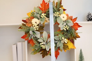 Detail of 45cm autumn wreath with maple leaves and pumpkins being measured on a shelf