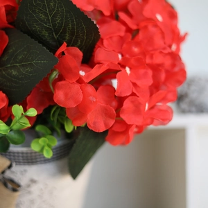 Artificial red geraniums in a vintage textured pot with a black and white plaid ribbon