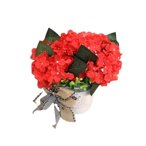 Artificial red geraniums in a white metal pot with a vintage logo and a burlap bow