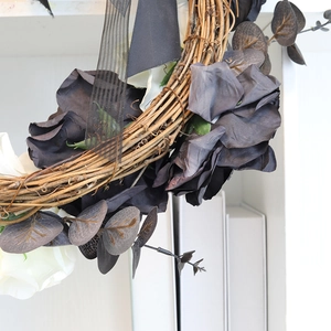 Gothic Halloween wreath with black roses and dark foliage on a minimalist white wall