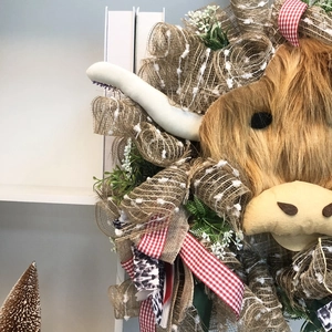 Spring decorative highland cow wreath with floral greenery and plaid ribbons on white shelf