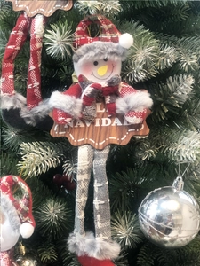 Detail view of hanging snowman plush with long legs and Feliz Navidad wooden sign