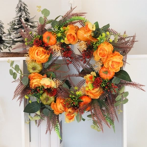 Detail of autumn wreath with orange roses, mini pumpkins, red berries and green foliage