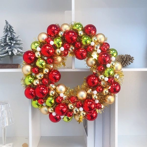 Detail of a Christmas wreath with red gold and green ornaments on a white shelf