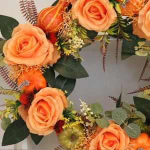 Close-up of autumn wreath with orange silk roses, realistic pumpkins and fall foliage