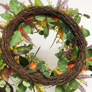 Detail of autumn wreath with orange pumpkins, green leaves and feathers on natural vine