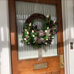 Artificial red and white tulip wreath with bow decoration on a rustic wooden door