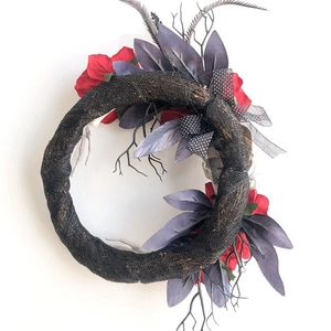 Halloween wreath with black branches, red roses, purple leaves, and a white skeleton hand