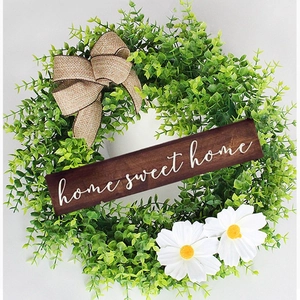 Detail of eucalyptus wreath with daisies and wooden sign saying home sweet home