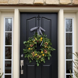 Artificial lemon and red berry wreath with striped bow on black door for home decor